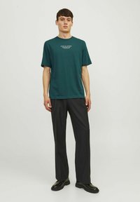 Vihreä puuvillainen t-paita lyhyillä hihoilla, jossa on valkoinen teksti "JACK & JONES PREMIUM". Yhdistetty mustiin, löysiin housuihin ja mustiin kenkiin.