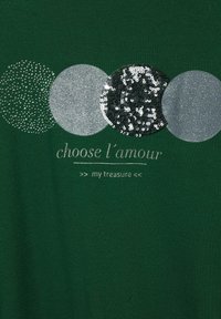 Grön t-shirt med fyra runda paljett detaljer i silver och svart, med texten "choose l'amour my treasure" i silver under.