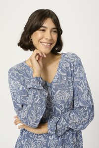 Blouse à motifs bleus en tissu léger, dotée d'un col en V, de manches longues avec des poignets froncés et d'intricate motifs floraux blancs.