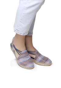 Scarpe espadrilles con una toma superiore in tessuto a strisce multicolori, con cinturini elastici e suola in juta intrecciata, abbinate a jeans chiari risvoltati.