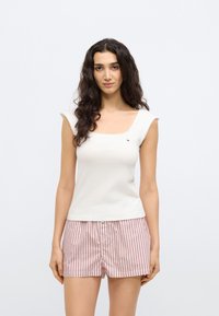 Biała dopasowana bokserka z kwadratowym dekoltem i krótkimi rękawami, zestawiona z jasnoróżowymi i białymi szortami w paski. Szczegóły logo na górze.