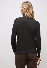 Dunkler Strickpullover mit hohem Halsausschnitt, langen Ärmeln und gerippten Bündchen. Der Stoff wirkt weich und glatt und bietet eine figurbetonte Silhouette.