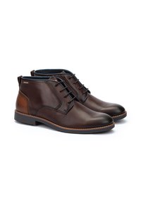 Botas de tobillo de cuero marrón oscuro con un acabado suave, cierre de cordones y acentos en el talón de color marrón más claro. Suela de goma con borde cosido.