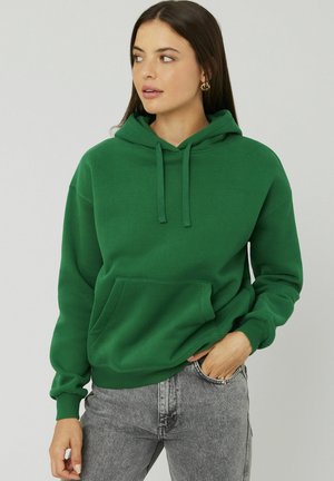 Sweat à capuche vert en matériau doux, avec une poche kangourou, des cordons ajustables et des poignets côtelés.