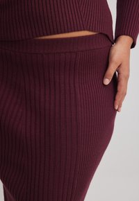 Burgundy ribbad stickad outfit som består av en åtsittande topp och en matchande kjol. Texturen är mjuk, med vertikala ränder som löper genom hela plagget.