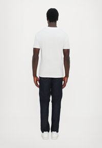 Hvit bomulls t-skjorte med korte ermer, kombinert med mørkeblå denimjeans. Standard passform, minimal design, med hvite joggesko.