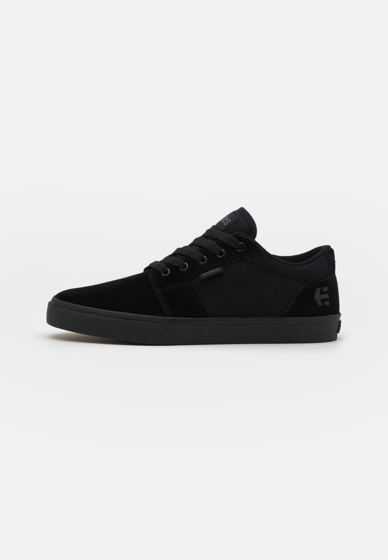 Black sneaker with a suede and canvas upper, round toe, flat rubber sole, and tonal laces. Features a small logo on the side.