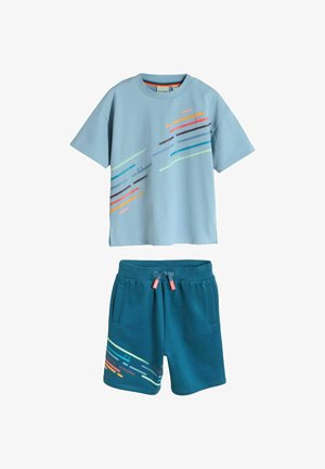 Hele sinine lühikeste varrukatega T-särk erk värviliste diagonaalsete triipudega, mida täiendab türkiissiniste nöörlindiga lühikesed püksid, mille vasakul jalal on sobiv triibumuster.