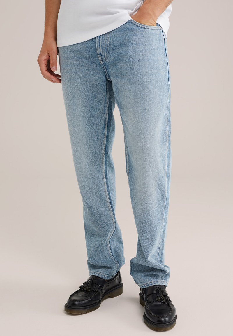 Lichtblauwe denim jeans met een recht model, zichtbare stiksels en een klassiek vijf-pocket ontwerp, gecombineerd met zwarte instappers.