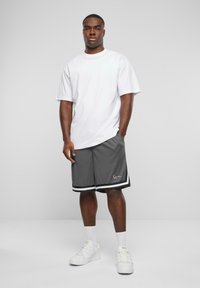 Vit t-shirt med kort ärm i kombination med grå shorts som har svart- och vitrandig design och en logotyp, fulländat med vita sneakers och ankelsockor.