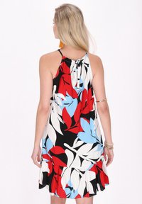 O rochie cu guler halter care are un model floral cu frunze roșii, albastre și albe pe un fundal negru, terminată cu un tiv ondulat.