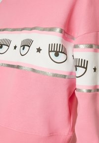 Sudadera rosa con una banda blanca que presenta ojos gráficos y pestañas, acentuada con rayas plateadas y estrellas negras. Material de mezcla de algodón suave.