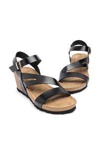 Sandali wedge neri in pelle con tre cinghie incrociate, soletta in sughero e suola in gomma texturizzata. Dettaglio in metallo dorato su una cinghia alla caviglia.