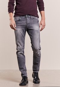 Szare jeansy z denimu z wyblakłymi łatami i przetarciami, zestawione z czarnymi skórzanymi butami i ciemnym swetrem.