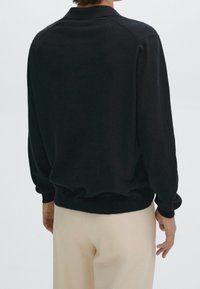 Zwarte pullover trui met een zachte textuur, geribbelde manchetten en zoom. Heeft een klassieke kraag en een ontspannen pasvorm, gestyled met lichtgekleurde broeken.
