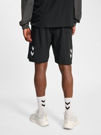 Isik, kes kannab musti spordipükse valgete Chevroni logodega, valgeid sokke mustade Chevronitega ja valgeid tenniseid, vaadatuna tagant.