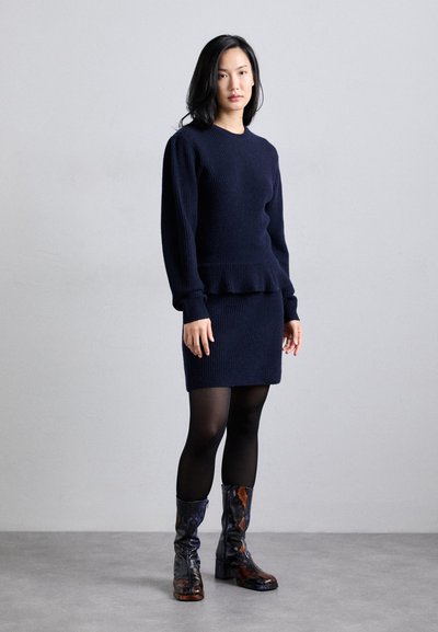 Suéter de punto azul marino con un dobladillo peplum, combinado con una falda de punto ajustada y medias negras. Lleva botas altas de textura en un patrón de piel de serpiente.
