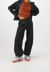 Svarta cargobyxor med flera fickor, kombinerade med en orange stickad tröja. Vita och orange sneakers fulländar outfiten.