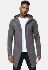 Cárdigan largo con capucha en color gris, hecho de una tela suave, que cuenta con una apertura frontal, bolsillos laterales y un diseño casual, combinado con una camisa blanca.