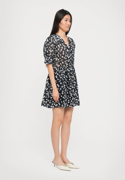 Rochie navy cu imprimeu de frunze albe, maneci scurte tip puff, decolteu în V, talie ajustată și fustă evazată. Asortată cu mules crem.