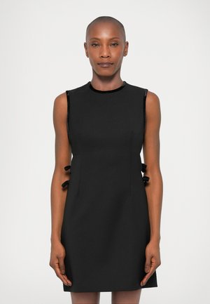 Vestido negro sin mangas con un escote alto, que presenta lazos laterales y una textura suave, ajuste entallado y longitud por encima de la rodilla.
