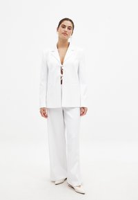 Valge bleiser sidumisega ees, mis on paaritatud laiade valgete pükstega. Sile kangas, struktureeritud disain ja minimalistlikud detailid.