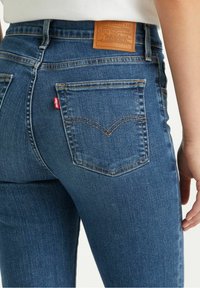 Vaqueros de mezclilla azul con un diseño ajustado, que cuentan con un parche de cuero de la marca en la cinturilla y un patrón de costura distintivo en el bolsillo trasero.