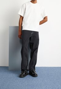 White short-sleeve t-shirt paired with dark gray loose-fit jeans featuring contrasting stitching. Black slip-on shoes with intricate design details.