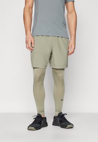 Set för herrar med sportkläder som består av en grå t-shirt, ljusgröna shorts och ljusgröna leggings med en svart Nike-logotyp. Svarta träningsskor.