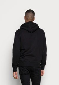 Sudadera negra con una gran capucha, puños y dobladillo acanalados. Fabricada con una tela suave, presenta un diseño limpio sin patrones ni logotipos visibles.