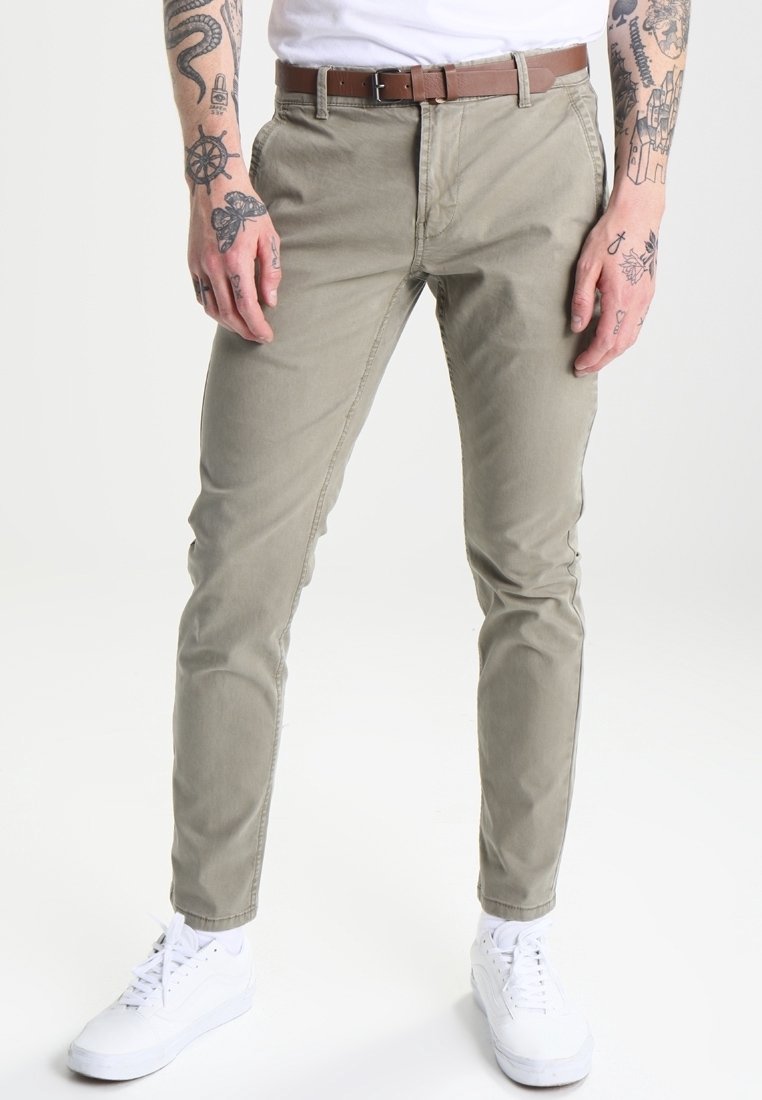 Chinos khaki avec une coupe slim, dotés d'une fermeture éclair, de poches avant et d'une ceinture en cuir marron. Associés à des baskets blanches.
