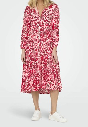 Robe à motifs rouges et blancs avec des manches longues, un devant boutonné et une jupe à volants. Portée avec des baskets blanches. Texture de tissu lisse.