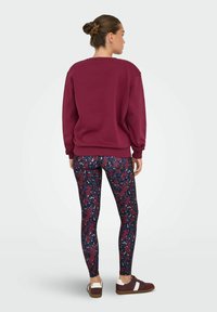 Bordeaux sweatshirt met een ronde hals, gecombineerd met gepatternde leggings met rode, marineblauwe en witte vlekken. Lage sneakers maken de look compleet.