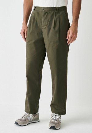Khaki green pleated pants with a straight cut, made of lightweight fabric. Features a button closure and side pockets. Worn with gray sneakers.