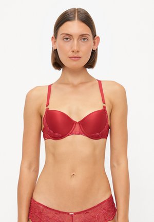 Red bra with padded cups, lace detailing along the edges, and adjustable straps. Features gold hardware accents and smooth texture.