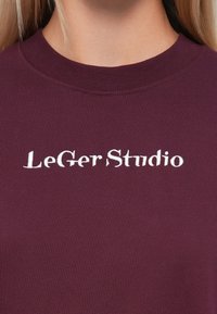 Burgundy ribbed cotton sweatshirt featuring white embroidered "LeGer Studio" logo across the chest, round neck design, and soft texture.