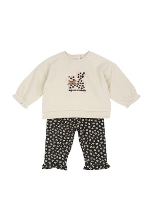 Haut crème à manches longues avec imprimé chat léopard noir et texte « doux comme un câlin », associé à un pantalon noir à imprimé floral avec ourlets volantés.
