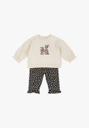 Haut crème à manches longues avec imprimé chat léopard noir et texte « doux comme un câlin », associé à un pantalon noir à imprimé floral avec ourlets volantés.