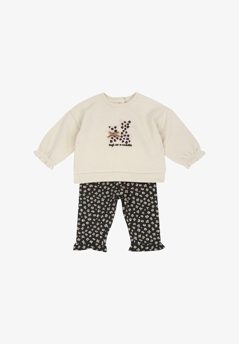 Haut crème à manches longues avec imprimé chat léopard noir et texte « doux comme un câlin », associé à un pantalon noir à imprimé floral avec ourlets volantés.