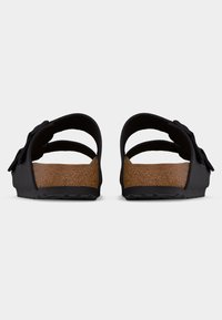 Οπίσθια όψη μαύρων σανδαλιών με πάτους φελλού και ρυθμιζόμενα λουριά σε ανοιχτό γκρι φόντο.