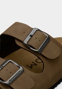 Sandali in pelle marrone con due fibbie metalliche regolabili, soletta imbottita e suola texturizzata per una maggiore aderenza.