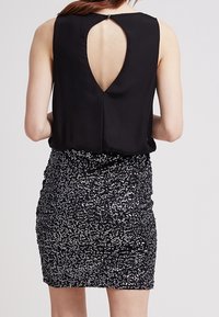 Haut noir sans manches avec un dos à ouverture en forme de goutte, associé à une jupe noire ajustée ornée de sequins et présentant un design texturé froncé.