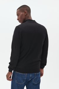 Black sweater with a crew neck and long sleeves, made from a soft knit material. Ribbed cuffs and hem. Worn with blue denim jeans.