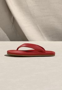 Czerwona flip-flop z wyściełanym paskiem o grubych paskach, umieszczona na jasnej powierzchni na tle z beżowego materiału.