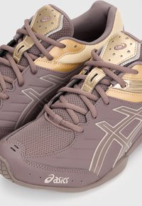 Ζεύγος μοβ και χρυσαφί αθλητικά παπούτσια Asics με διάτρητο επάνω μέρος, κορδόνια και λογότυπο της εταιρείας στο πλάι και στη γλώσσα.