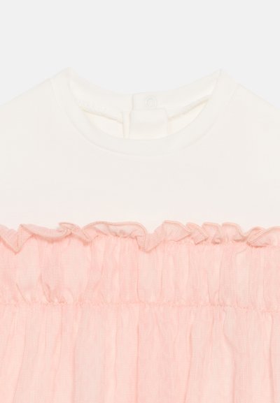 Top bianco con scollatura rotonda e sovrapposizione di chiffon rosa con volant sul petto.