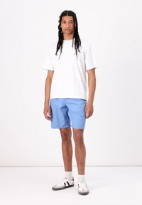 Camiseta blanca de manga corta y pantalones cortos azul claro, con un ajuste relajado. La persona lleva zapatillas blancas con rayas negras.