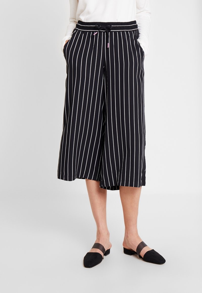 Svartvita vertikalt randiga culotter med elastisk midjeband och fickor, med en lös passform och lätt tygtextur.