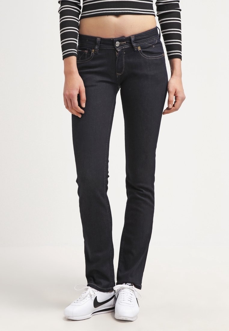 Jeans ajustados de denim azul oscuro, con una cintura media, costuras sutiles y diseño de cinco bolsillos, combinados con zapatillas blancas.
