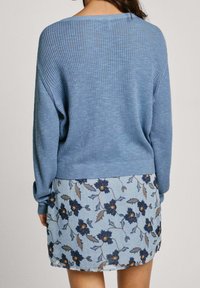 Maglione blu a coste con maniche lunghe abbinato a una gonna a fiori blu chiaro con motivi floreali navy e dettagli marroni.